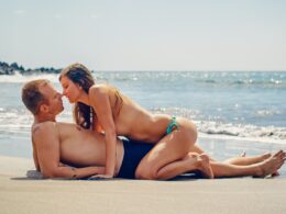 Man Lying on Sand While Woman Kissing Him