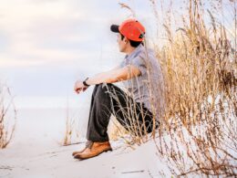 man sitting on sand with wheat looking right during daytime