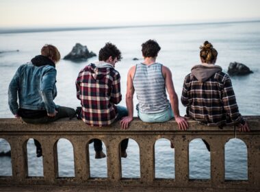 four person sitting on bench in front of body of water